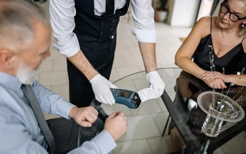 A couple making a contactless payment using a credit card at a restaurant table.