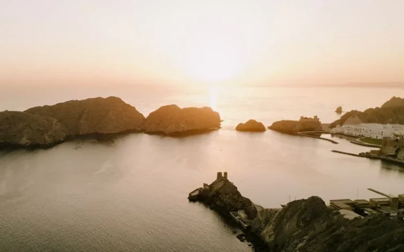 Beautiful aerial view of Oman's rocky coastline and serene sea during a golden sunset, enhancing the natural beauty of Muscat.