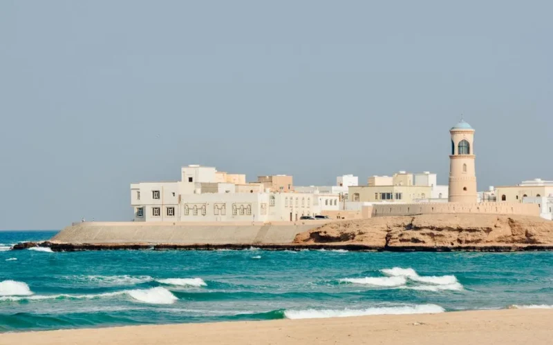 A serene view of Sur Lighthouse and traditional buildings on the Omani coast.