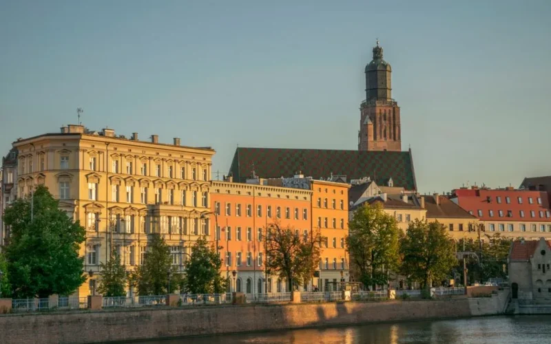 Capture of Wrocław's colorful townhouses and historic church by the Odra River at sunset.
