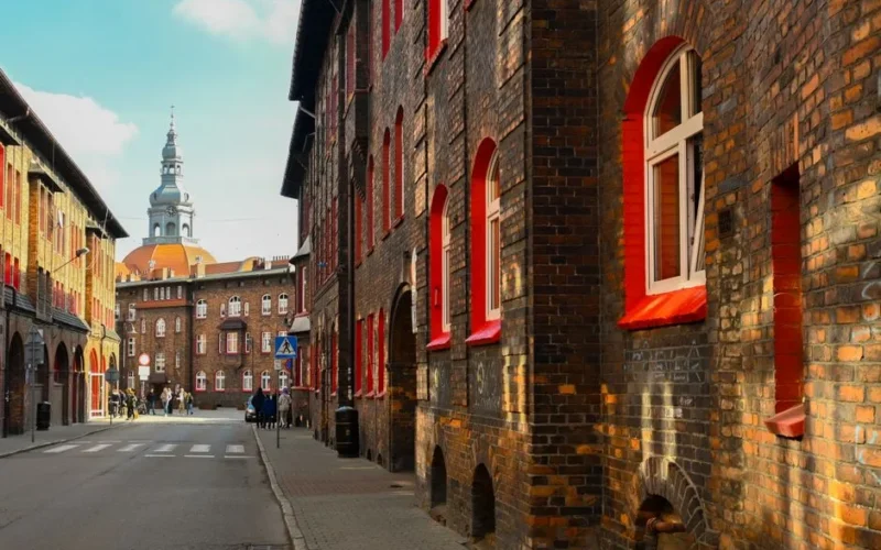 A picturesque street view featuring historic European buildings with red accents under a bright sky.