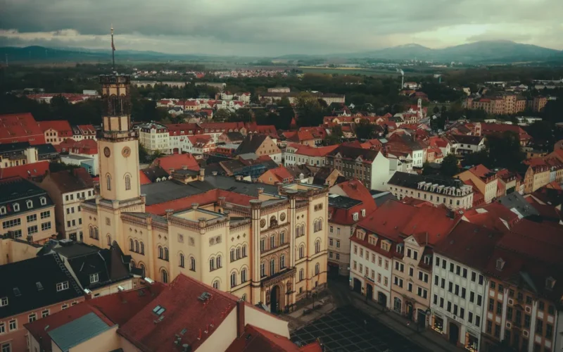 Drone shot of Zittau Town Hall surrounded by red-roofed buildings under cloudy skies.