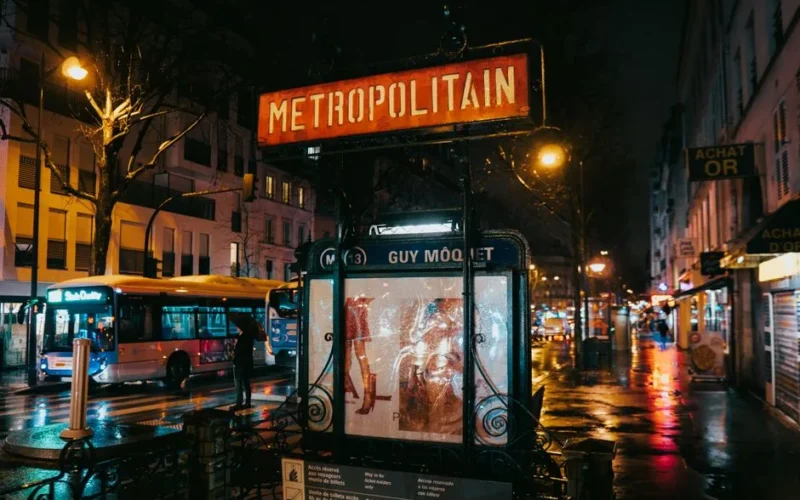 A wet Paris street captures the glow of city lights by the Metropolitain entrance at Guy Môquet metro station.