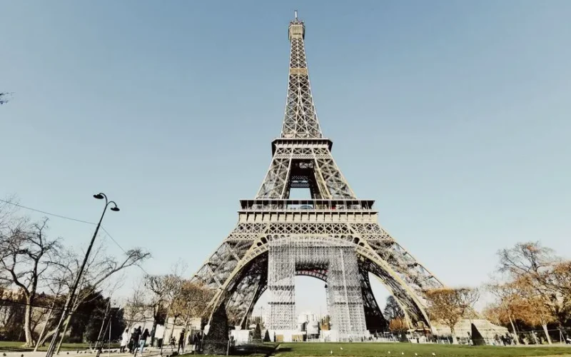 Low angle shot of the Eiffel Tower in Paris with blue sky and partial park view.
