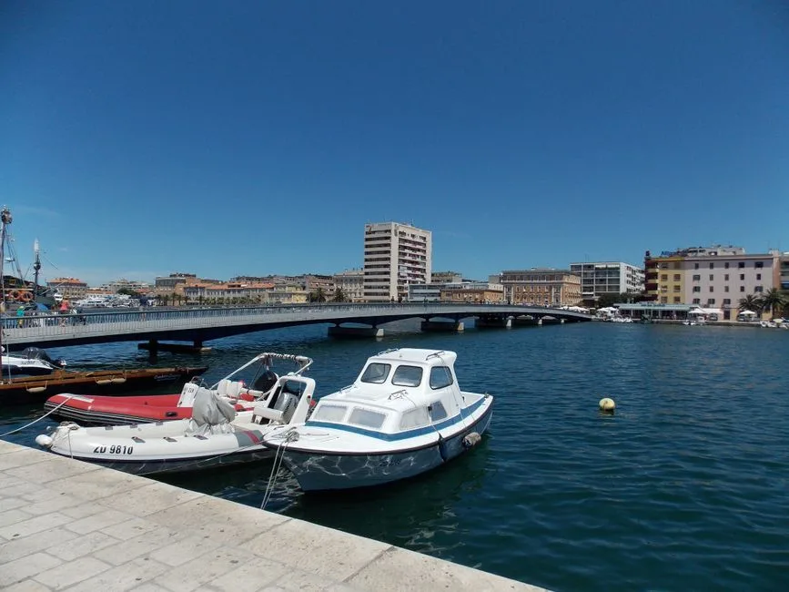 A picturesque view of Zadar harbor with boats and a bridge under a clear blue sky.