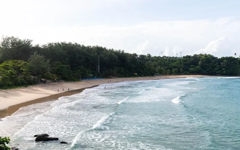 A serene beach with gentle waves and lush greenery in Phuket, Thailand.
