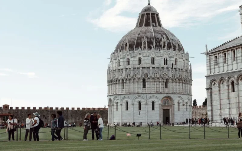 View of the San Giovanni Baptistery in Pisa with tourists, showcasing its architectural beauty.