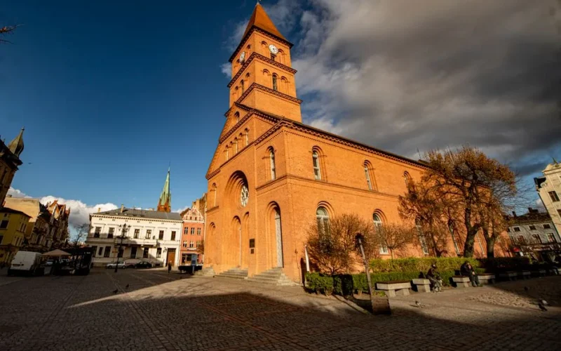 A magnificent red brick church dominates the lively town square under a dramatic sky.