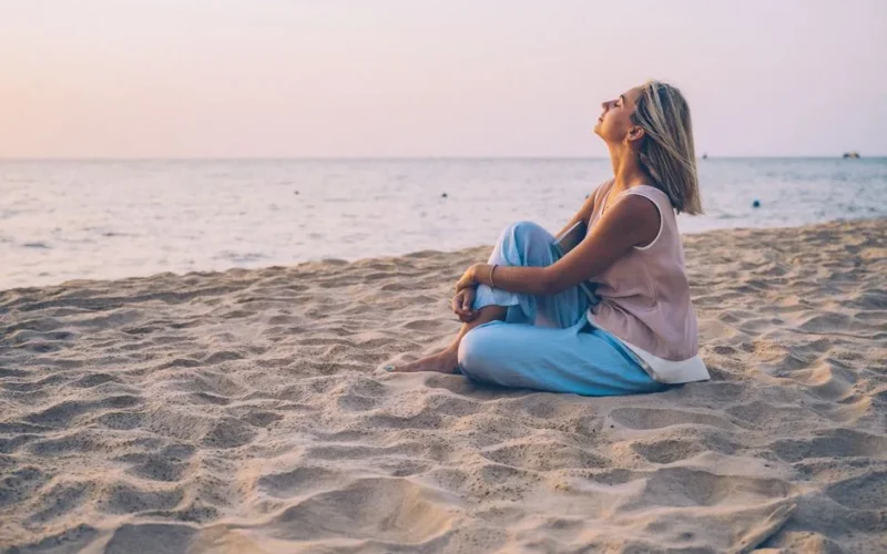 A peaceful moment as a woman relaxes on a sandy beach, enjoying the sunset.