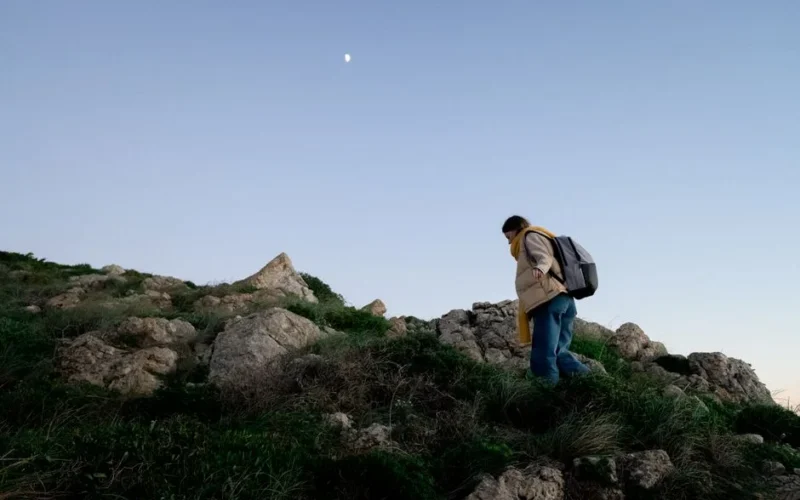 A woman hiker ascends a rocky hill under the evening sky, capturing a sense of adventure.