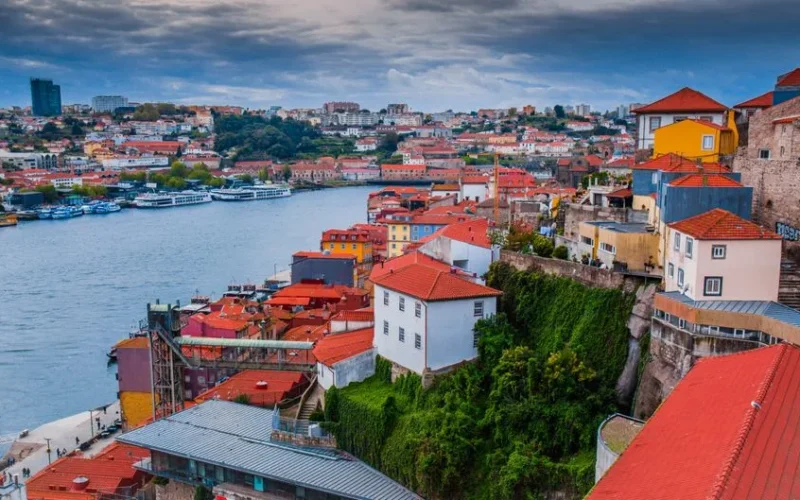 Scenic aerial view of Porto's vibrant riverside buildings along the Douro River under cloudy skies.