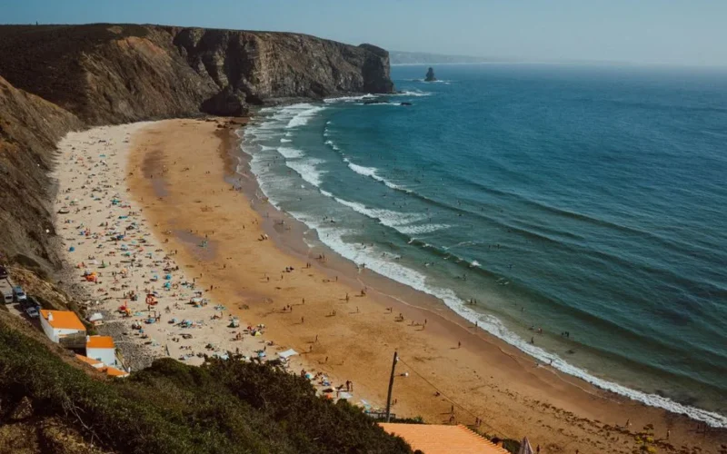 Breathtaking aerial view of a sunny beach along Portugal's Algarve coastline with turquoise waves & golden sand.