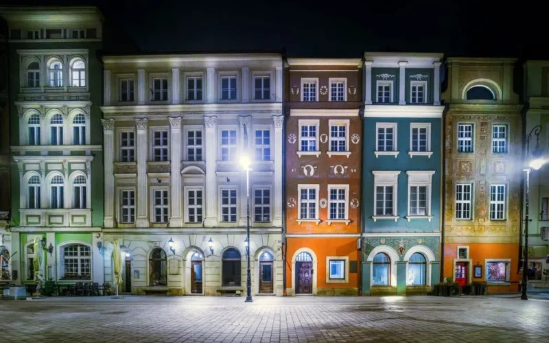 Vibrant townhouses illuminated at night in Poznań's historic Old Market Square.
