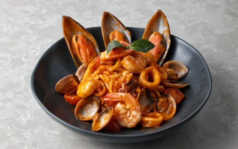 Mouthwatering seafood pasta with shrimp and mussels in a black dish on a gray surface.