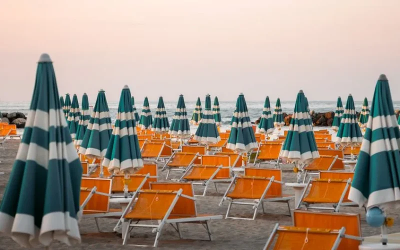 Colorful striped umbrellas and chairs on Rimini beach during sunset, perfect for summer vibes.