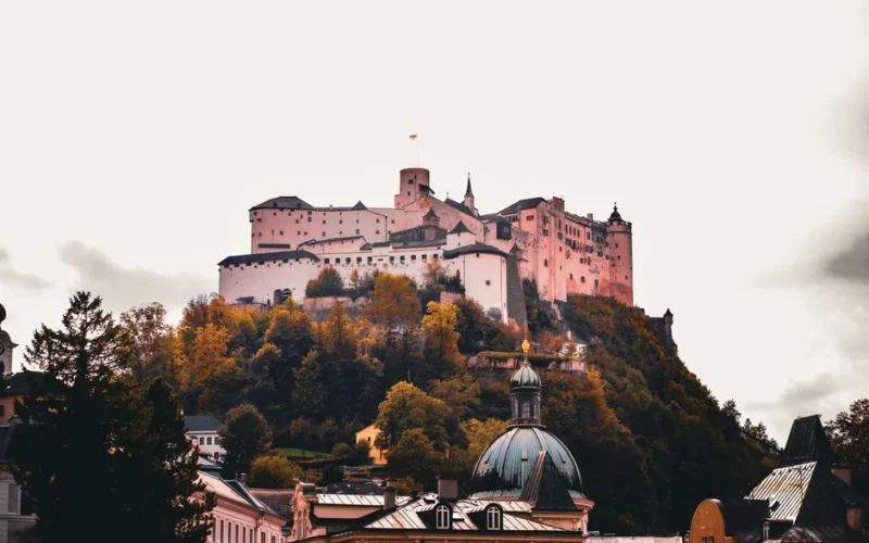 View of the Hohensalzburg Fortress atop a hill surrounded by vibrant autumn foliage in Salzburg, Austria.
