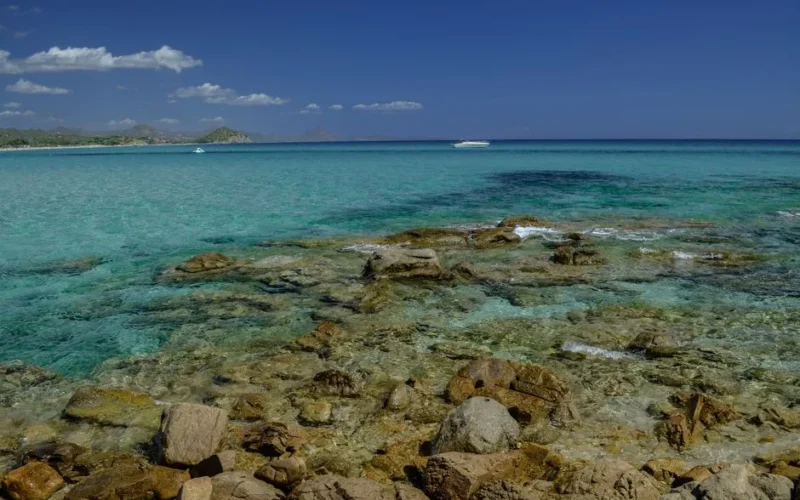 Stunning clear turquoise waters and rocky shores of a Sardinian beach under a bright blue sky.