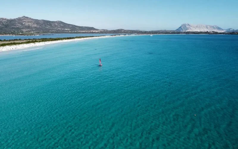Stunning aerial view of Sardinia's turquoise waters with distant mountains and clear skies.
