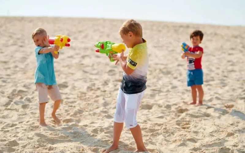 Kids having fun with water guns on a sunny beach day.