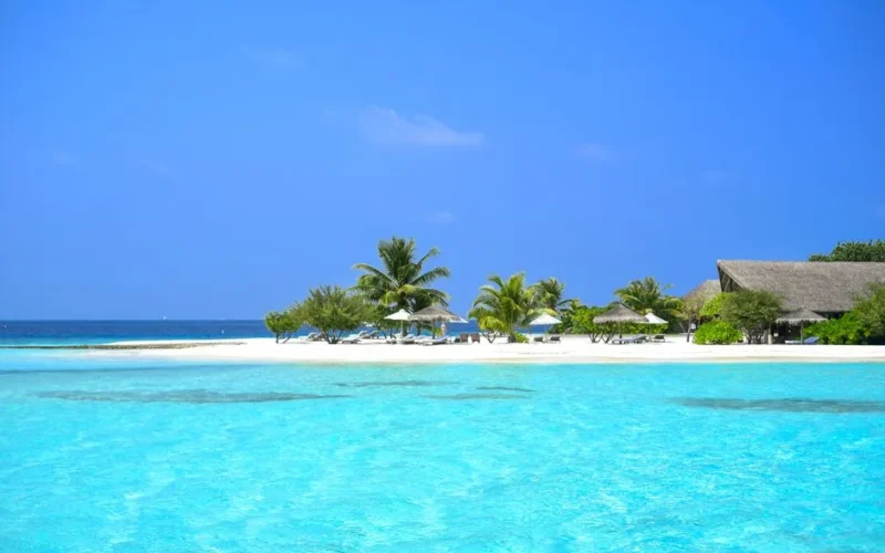 Stunning tropical beach with clear blue water, palm trees, and resort huts, perfect for a relaxing holiday.