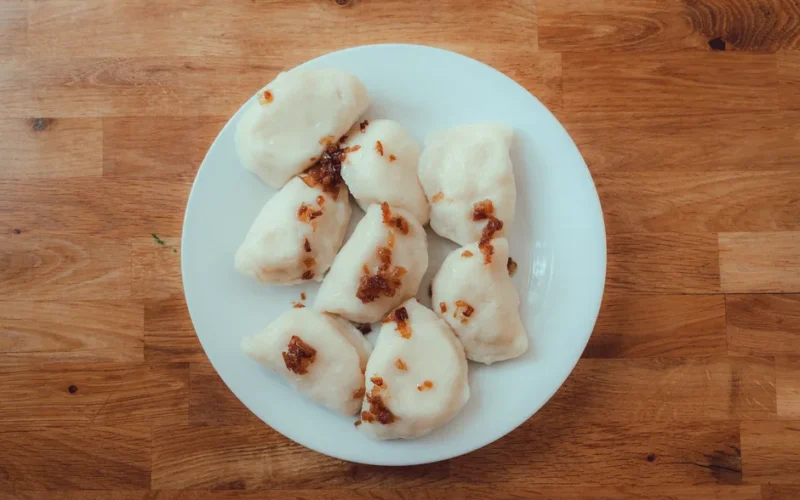 Plate of homemade Polish pierogi with crispy onions on wooden table