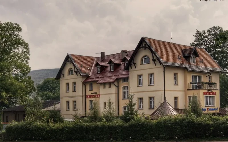 Elegant hotel in Świeradów-Zdrój, Poland with classic architecture amidst lush greenery.