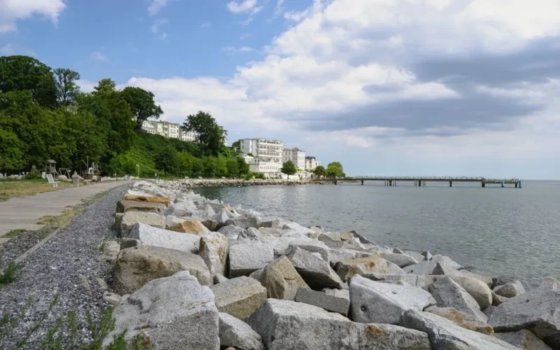 Idyllic coastal landscape featuring a promenade, pier, and lush greenery along the seashore.