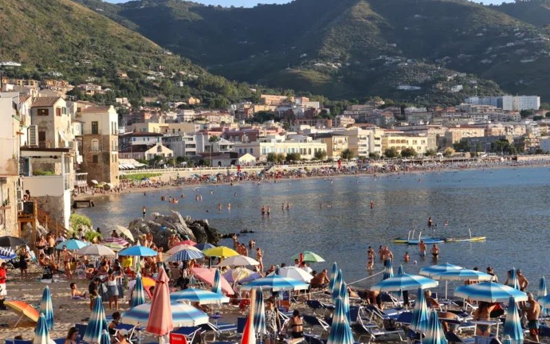 Vibrant summer day on Cefalù beach, Sicily with sunbathers and scenic coastal backdrop.