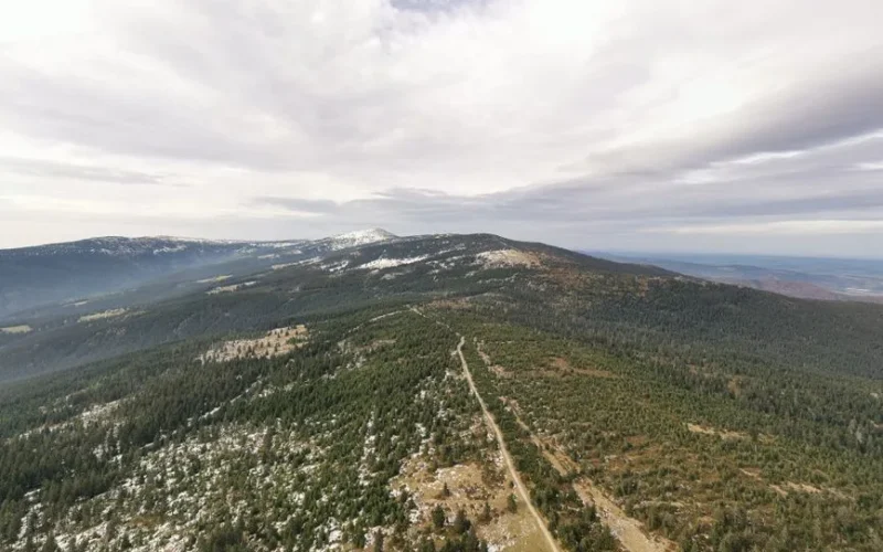 Stunning aerial shot of Krkonoše Mountains with snow patches and lush forests.