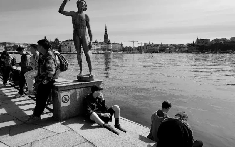 Black and white view of Stockholm's waterfront with people enjoying the promenade.