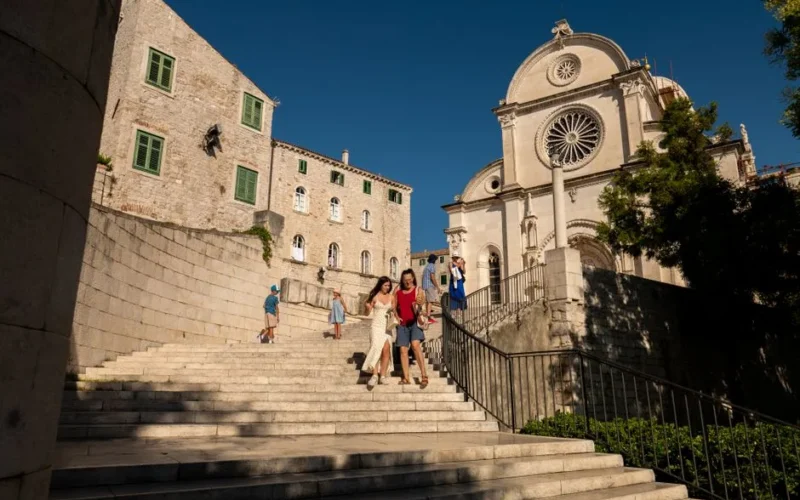 Tourists walking down the historic stairs by St. James Cathedral in Šibenik, Croatia on a sunny day.