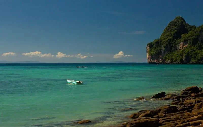 Idyllic Ao Nang beach scene with clear turquoise waters and lush green cliffs in Krabi, Thailand.