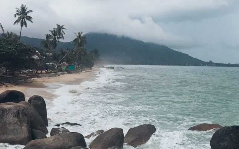 Serene view of a tropical beach in Koh Samui, Thailand, with crashing waves and lush greenery.