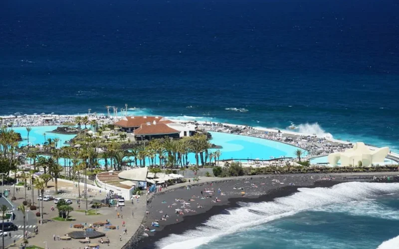 A stunning aerial shot of a coastal resort with black sand beach and blue ocean in Tenerife.