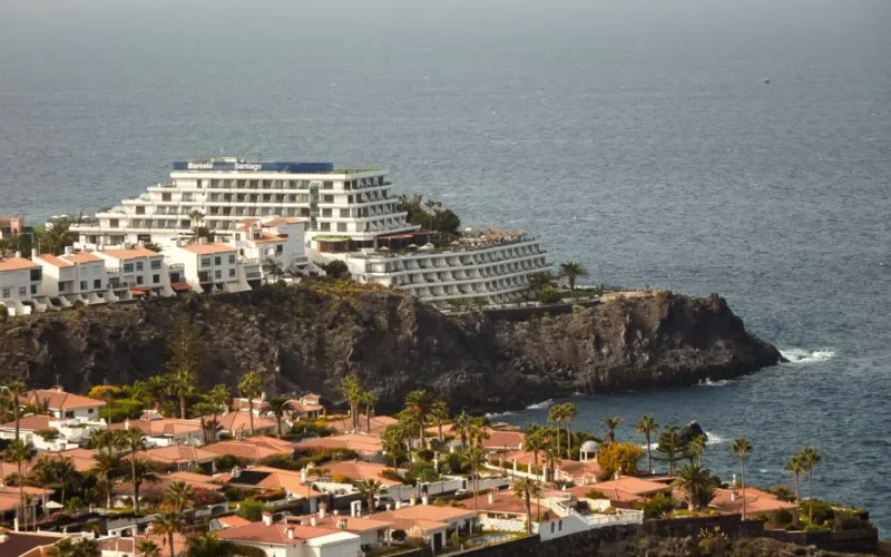 Aerial view of a stunning seaside resort on a cliff with ocean backdrop and palm trees.