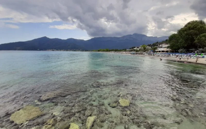 Experience the serene beauty of Chrisi Ammoudia beach in Greece with turquoise waters and lush mountains.