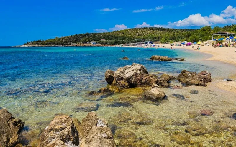 Idyllic beach scene in Thassos, Greece with blue waters and rocky shoreline under a sunny sky.