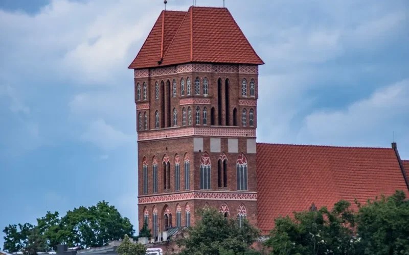 Majestic Gothic church tower in Toruń, Poland, under a bright blue sky, showcasing stunning architectural details.