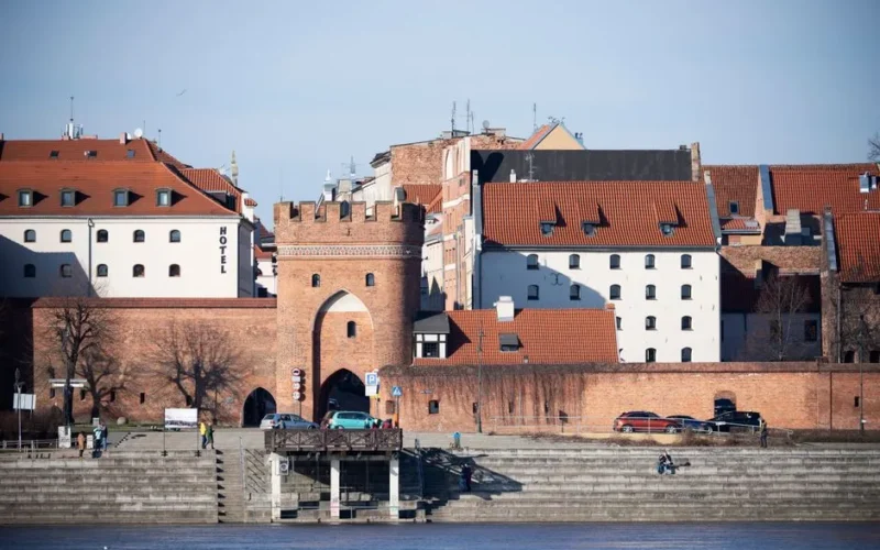 Toruń's medieval city gate by the riverside, showcasing red-brick architecture and urban charm.