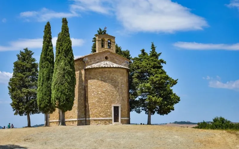 The picturesque Chapel of Vitaleta nestled in the serene Tuscan countryside with lush trees.