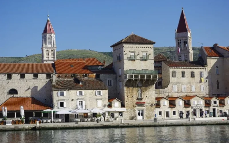 Explore Trogir's charming waterfront featuring medieval architecture and vibrant cafes under a clear blue sky.