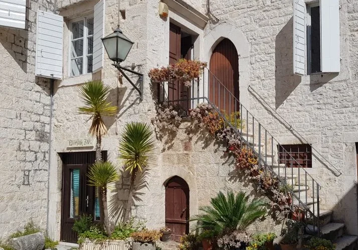Charming stone facade of a historic house in Trogir, Croatia featuring potted plants and classic architectural details.