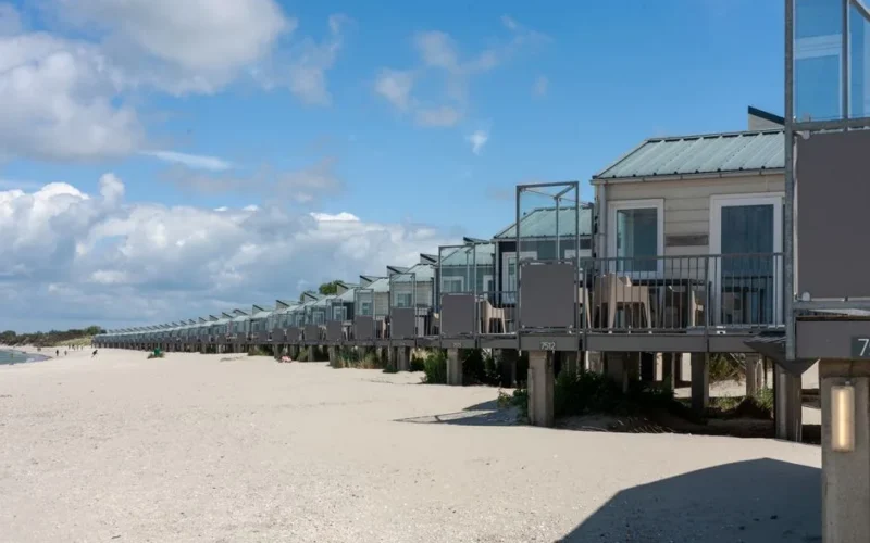 Row of modern beachfront cabins on a sunny sandy coastline under a blue sky.