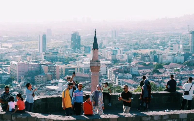 Tourists explore a historic site in Ankara with a panoramic city view, capturing blend of heritage and urban life.