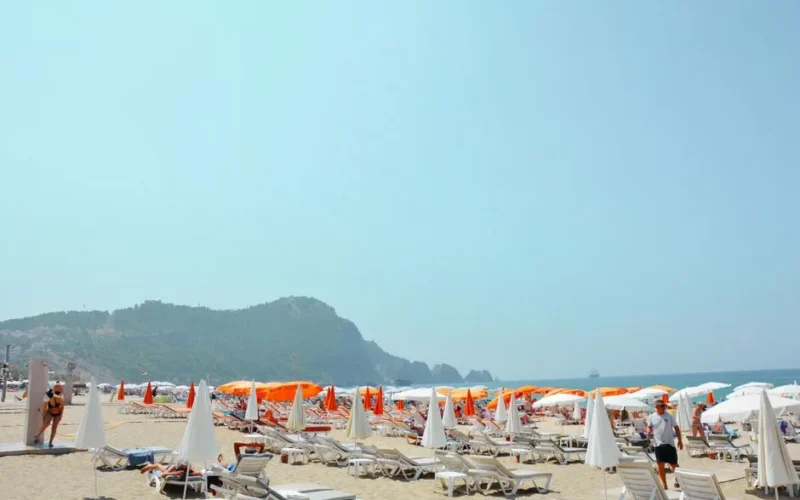 A vibrant summer day at a popular beach in Türkiye with sunbeds and umbrellas.