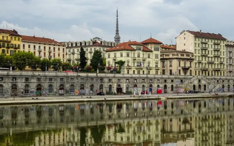 Scenic view of Turin's historic architecture reflected in the river under an overcast sky.