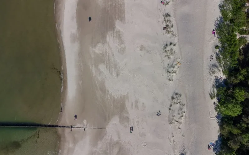 Bird's eye view of a sandy beach and shoreline in Ustka, Poland, with people walking.