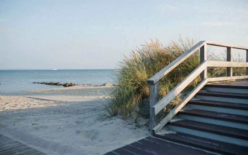 Scenic view of a wooden pathway leading to a tranquil sandy beach with gentle ocean waves.