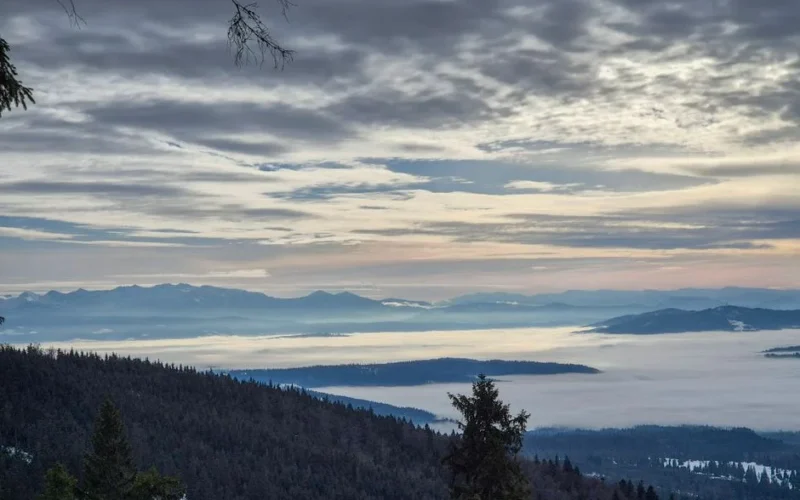 Serene winter view of mist-covered valleys and mountain range in Poland, under dramatic skies.