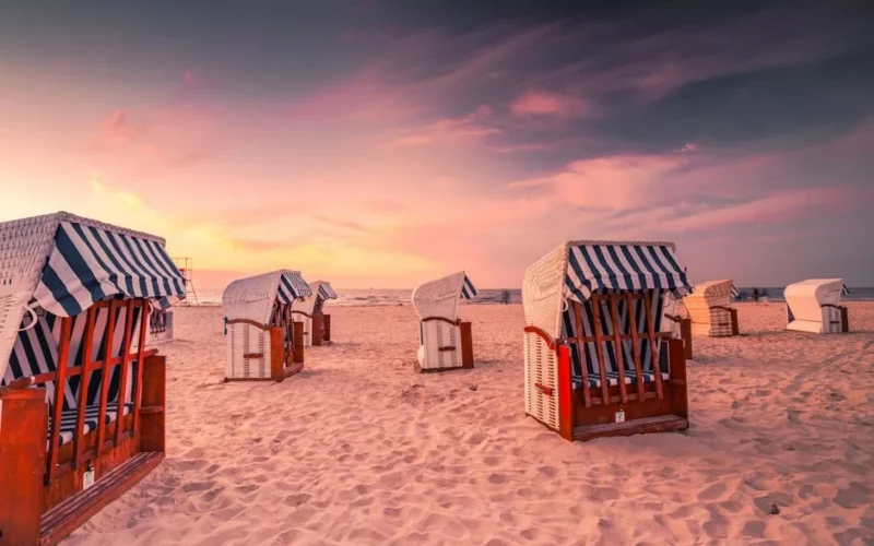 Relaxing beach scene with striped chairs and a vibrant evening sky in Świnoujście, Poland.